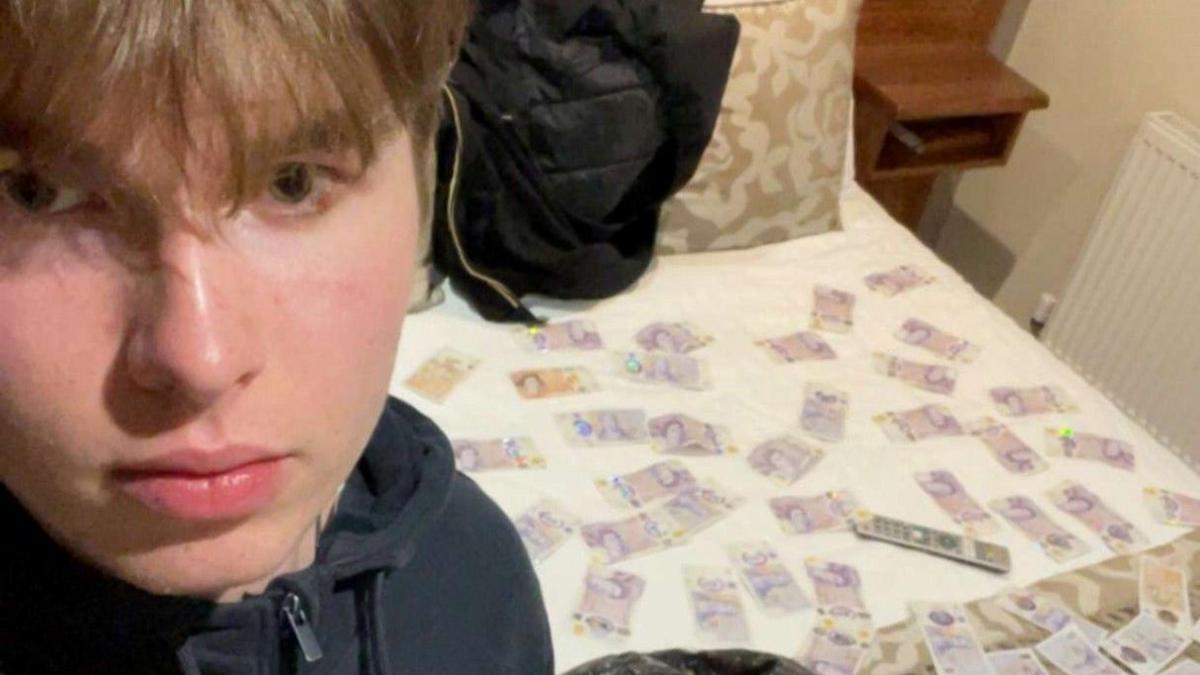 A boy with his face near the camera and a hotel bed in the background with lots of £20 notes spread out on it. 