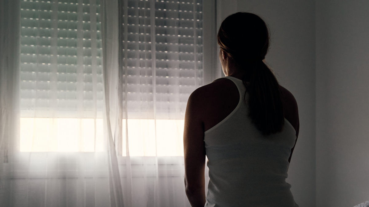 Rear view of an unrecognisable woman sitting on her bed looking out of a window