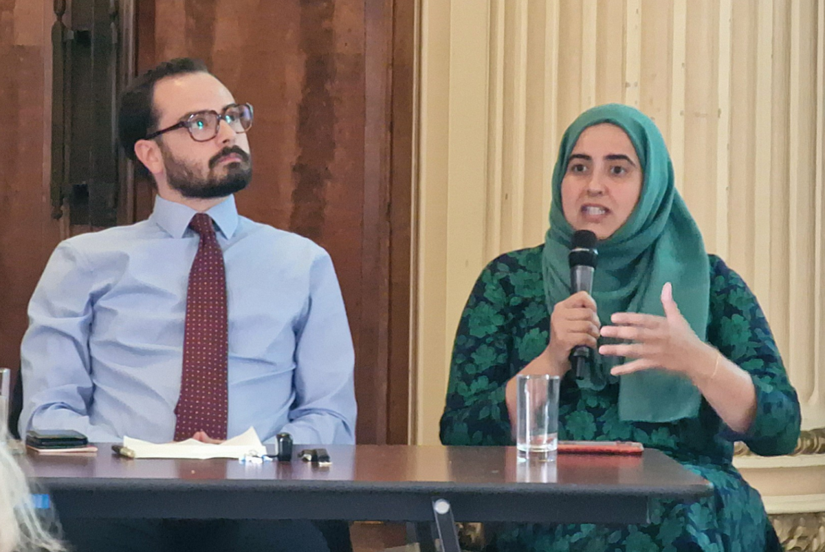 A man in a shirt and tie sitting next to a woman, wearing a headdress and talking into a microphone. 