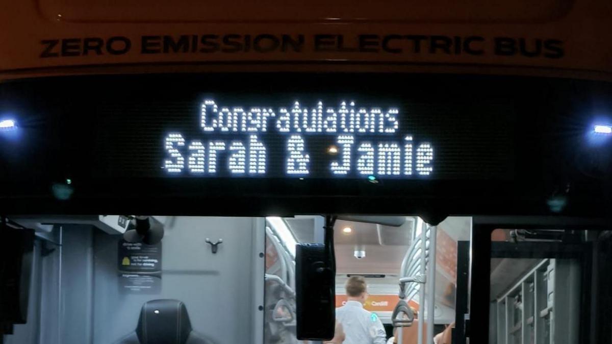 A bus with an illuminated sign on the front which says 'Congratulations Sarah and Jamie' 