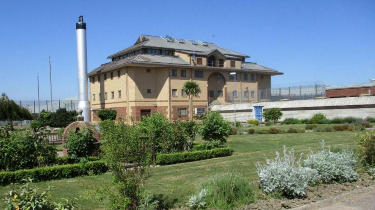 A large building on the other side of a grassy area. There are barbed wire fences on the horizon.