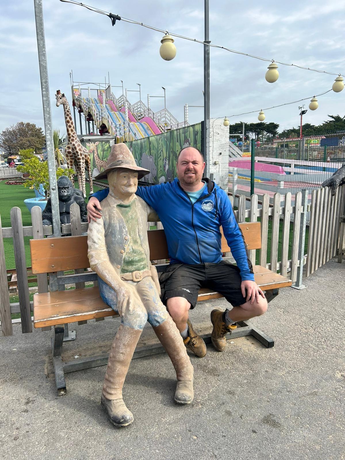 A man hugging a life sized statue of a man wearing a wide-brimmed hat and brown boots