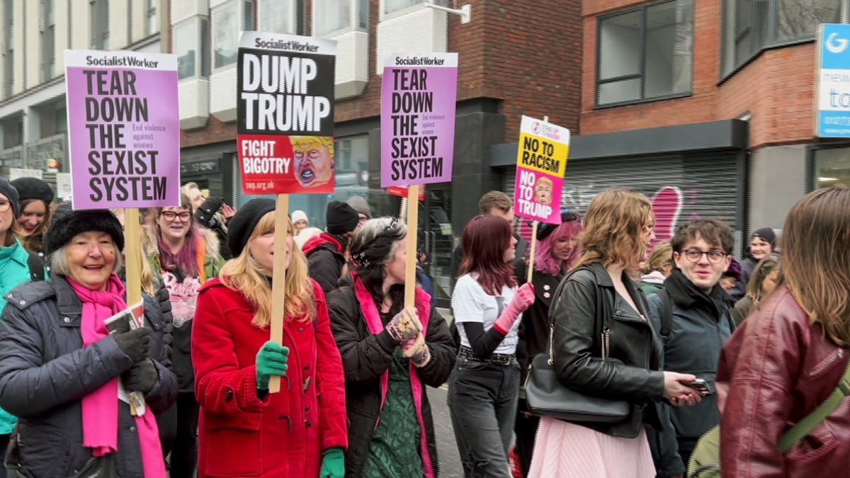 Women hold placards that read 'tear down the sexist system' and 'dump trump' as they wear bright colours and walk together through the streets of Brighton