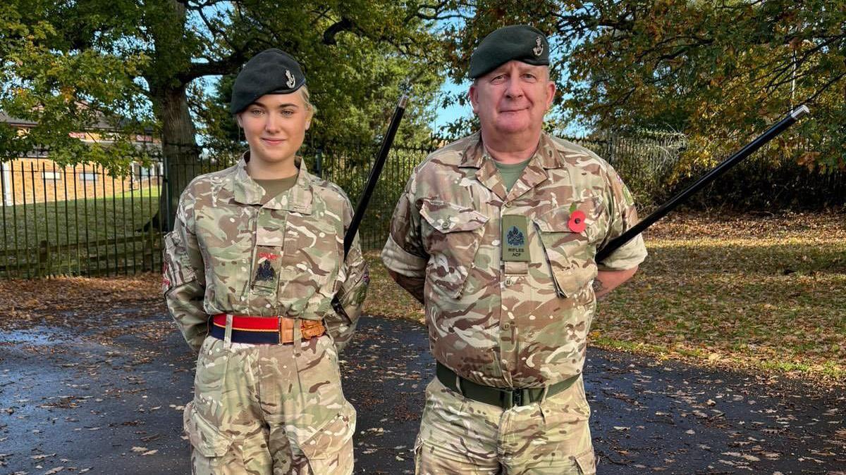 Arabella Mason pictured left with a male Army Cadet Force staff member on the right. They are both standing in a park wearing camouflage uniform and dark green berets