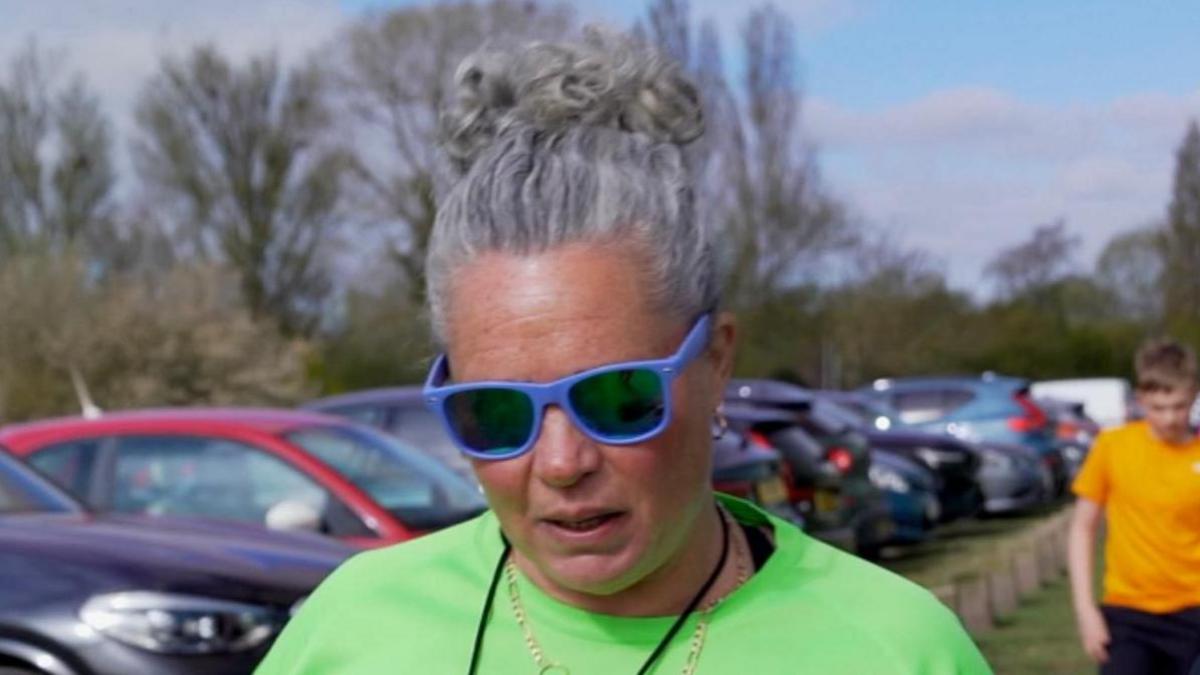 Sophie is wearing a lime green running T shirt, with her hair tied up in a bin, and has Blue framed sunglasses on. She also has a whistle around her neck, which is used to start and stop the groups running intervals.