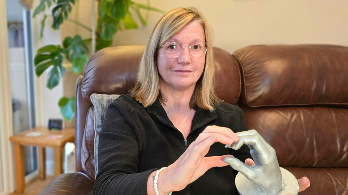 Christine Debney, holding her hand against a sculpture of another hand to form the shape of a heart