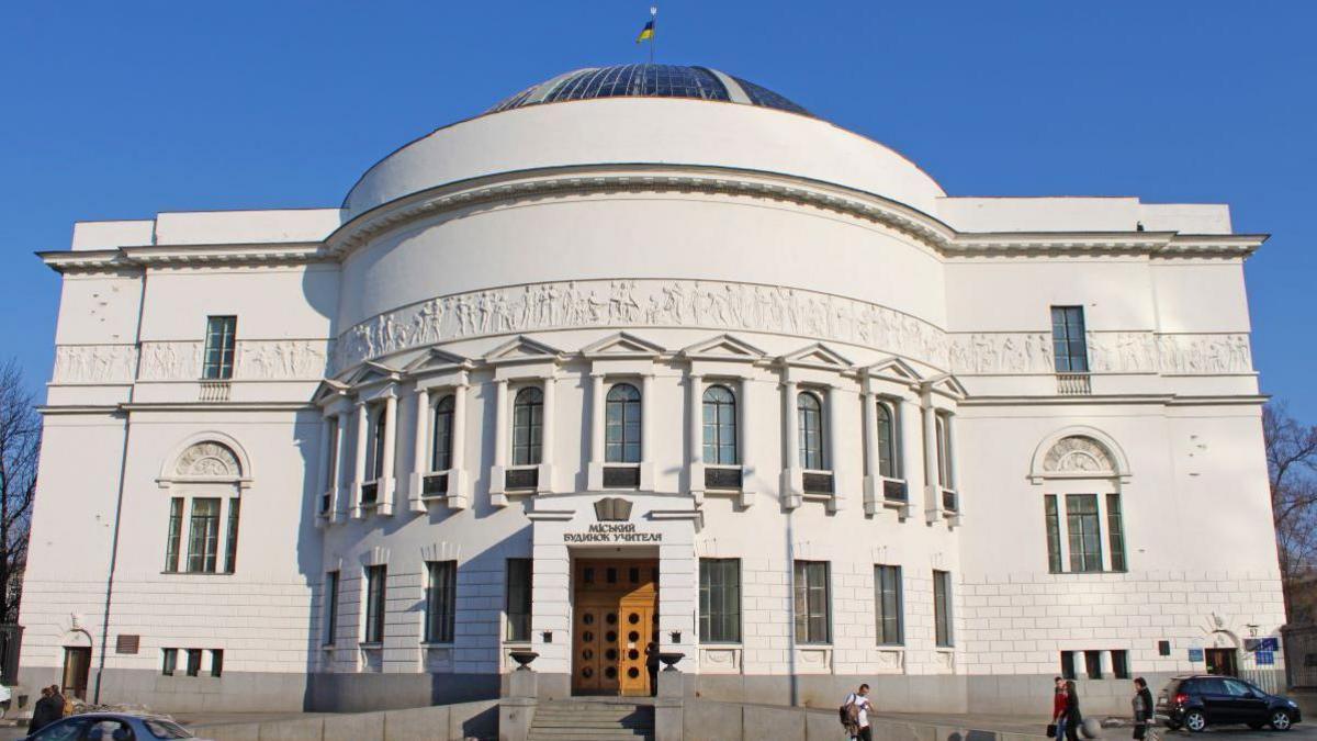 A rectangular white stone building with a curved feature at the front and a dome shaped roof. There are 17 windows across the curved part and a further 4 windows on the flat front of the building. There are steps up to a double wooden door.