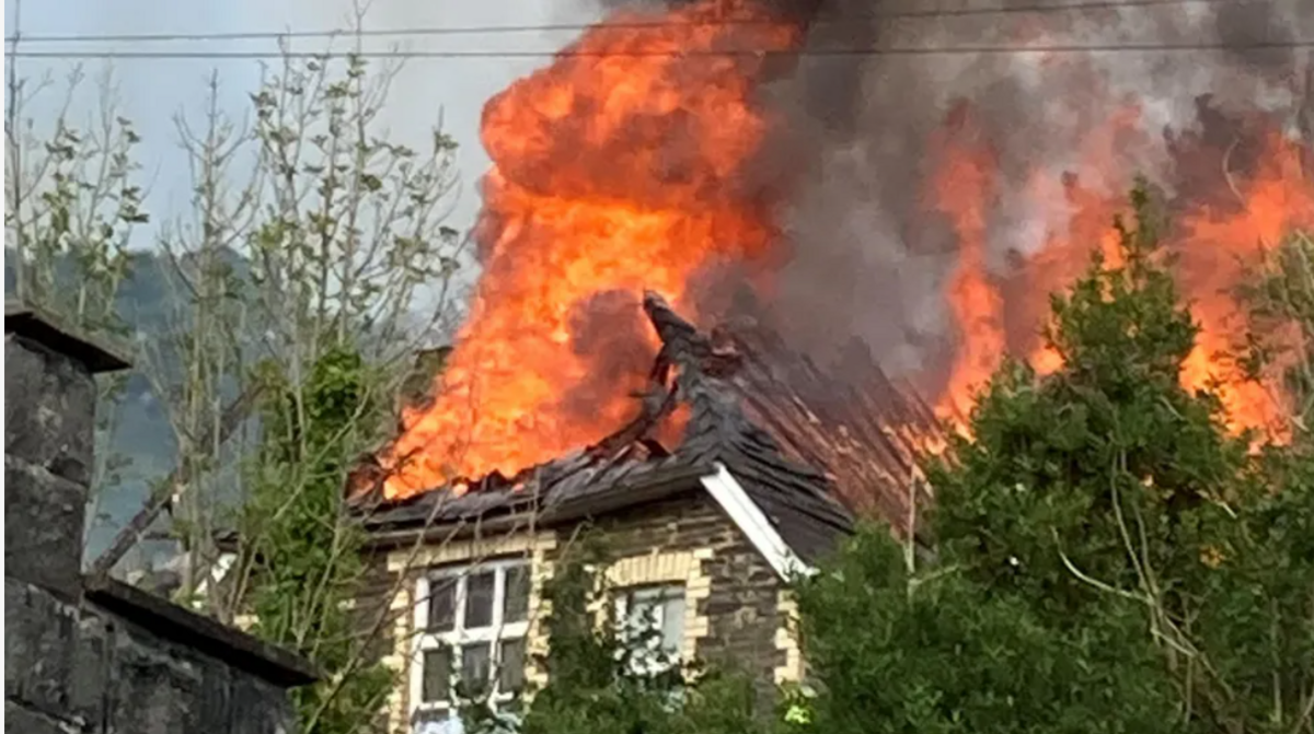 A close-up of the abandoned school building with huge orange flames and smoke billowing from the roof