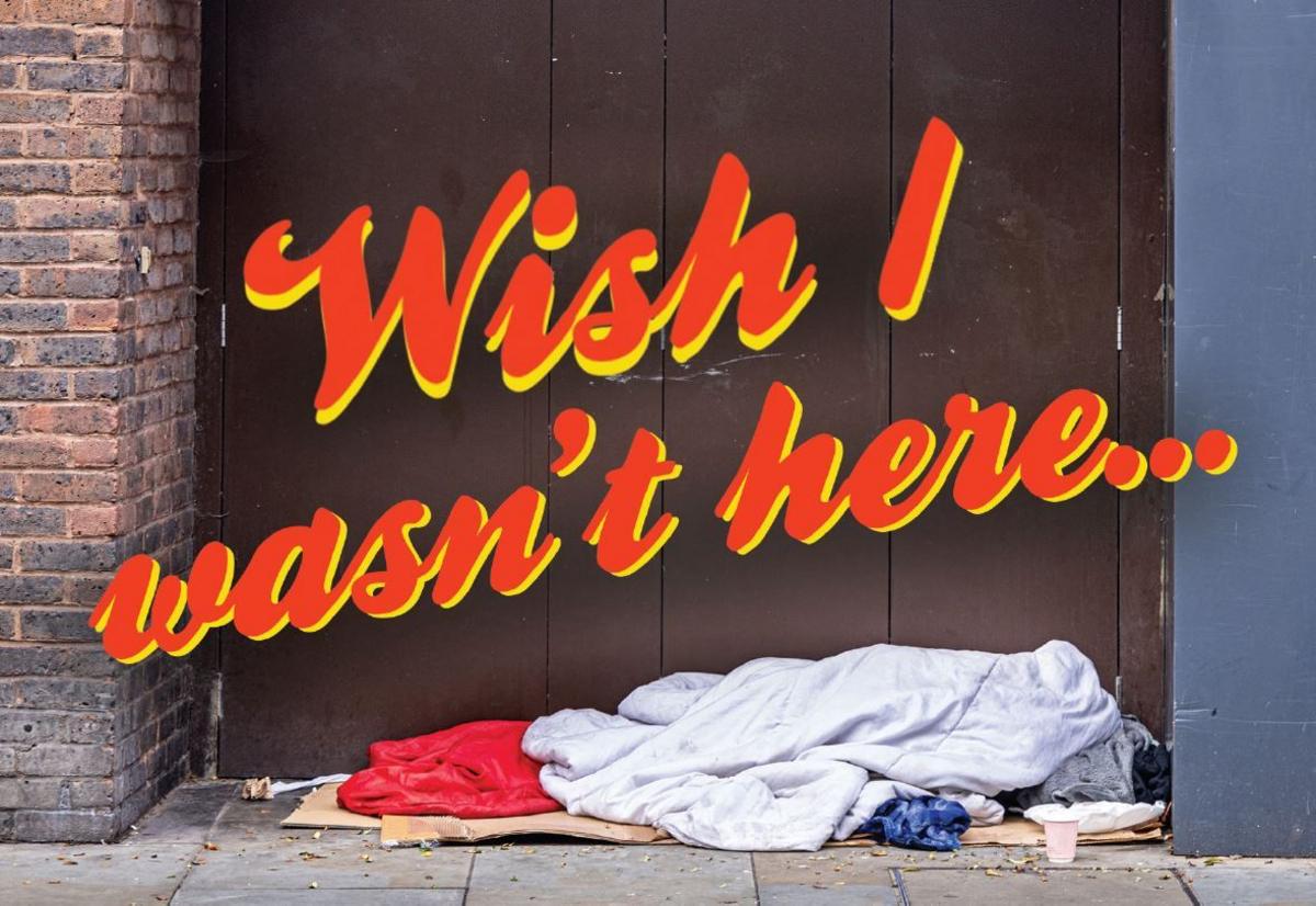 A postcard depicting clothes and blankets on cardboard on a floor. The words wish I wasn't here are written above in red and yellow