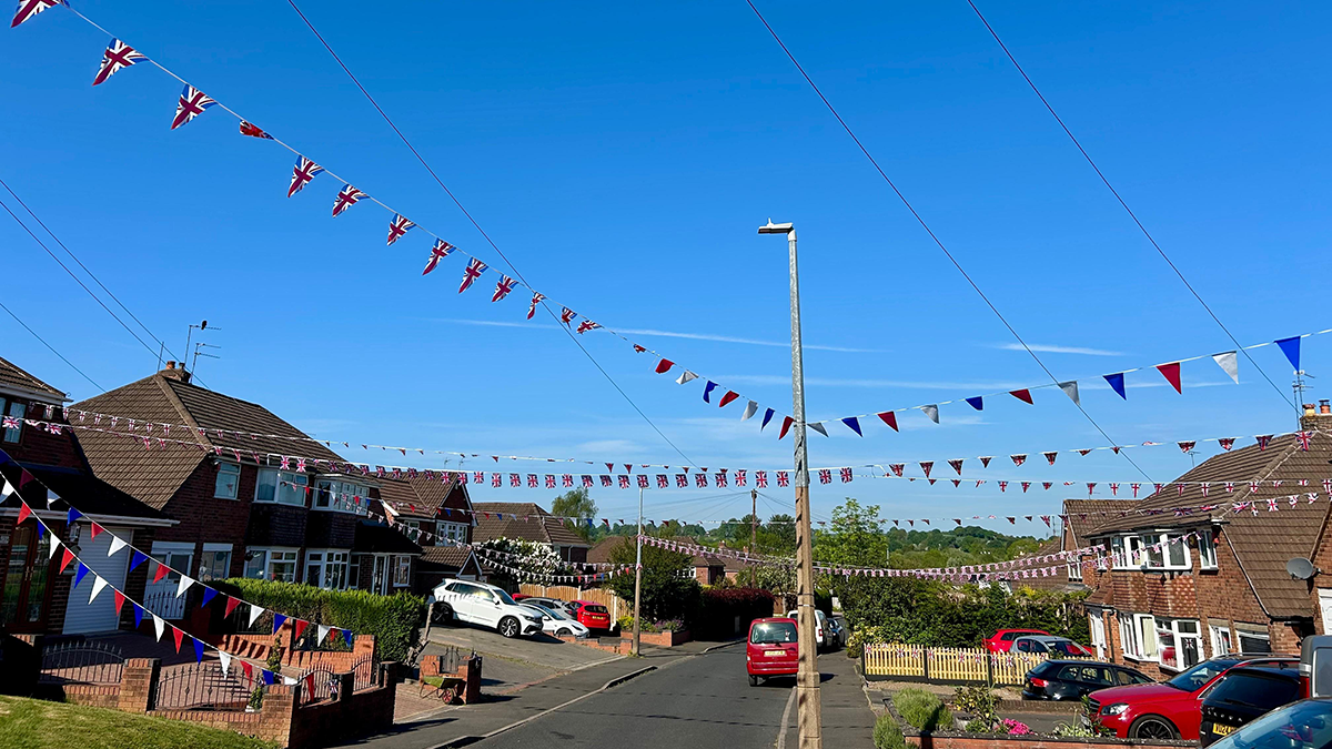 Bunting strung over a street, with cars parked on drives.