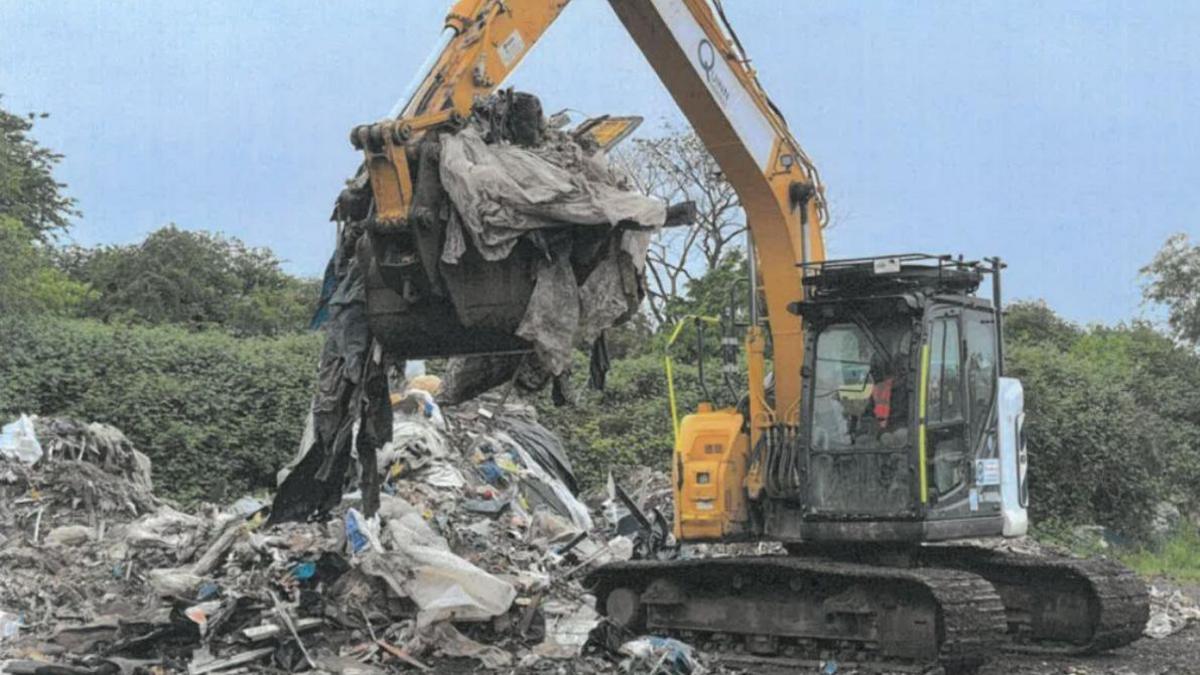 A digger is lifting piles of waste from land 