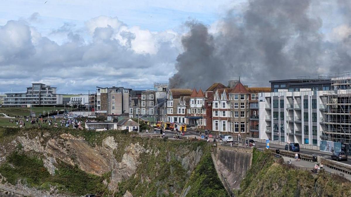 A large plume of black smoke comes from the roof on an multi-storey Victorian hotel on a Cornish clifftop, surrounded by others.