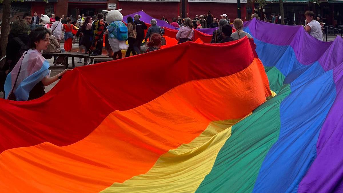 Pride attendees carry large rainbow flag through Oldham