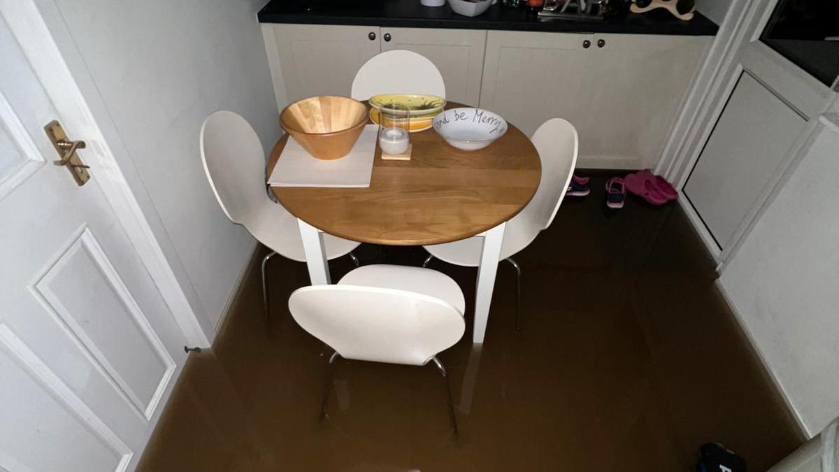 Brown water has seeped across a kitchen floor with four white chairs around a wooden circle table 