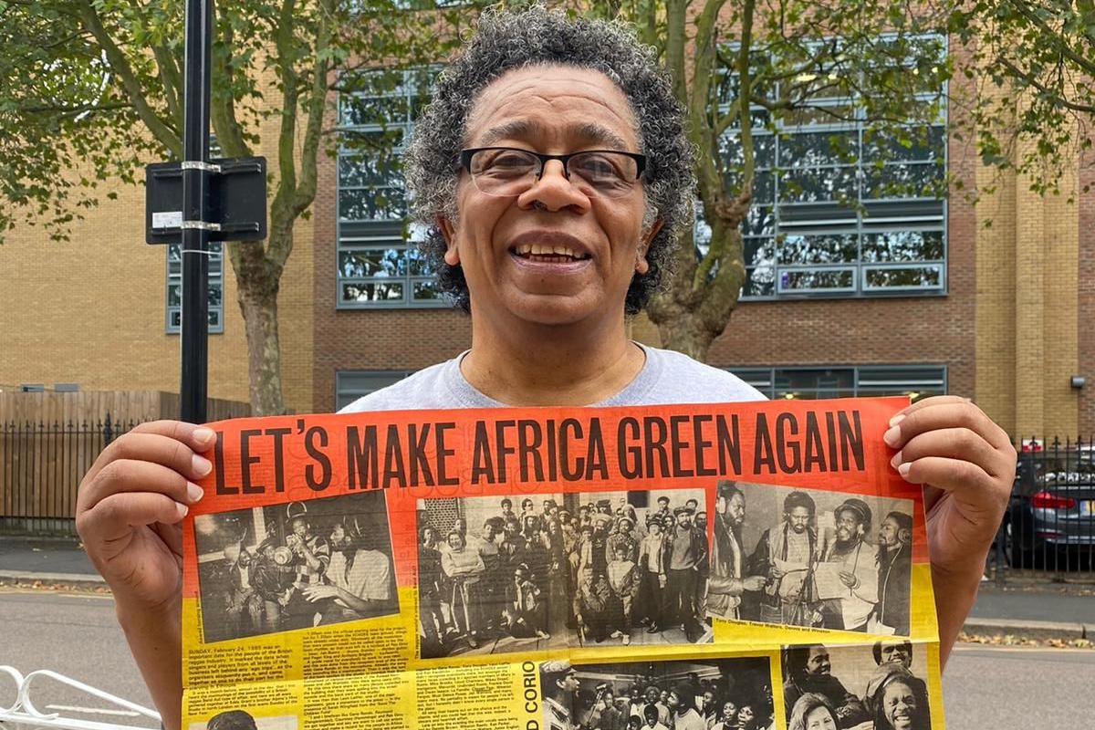 Leon Leiffer wearing glasses and a grey T-shirt holding up a newspaper page with Let's Make Africa Green Again written across the top