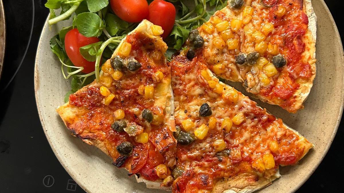 A tomato and cheese topped pizza on top of a mushroom base. It's served on a plate with a side of salad.