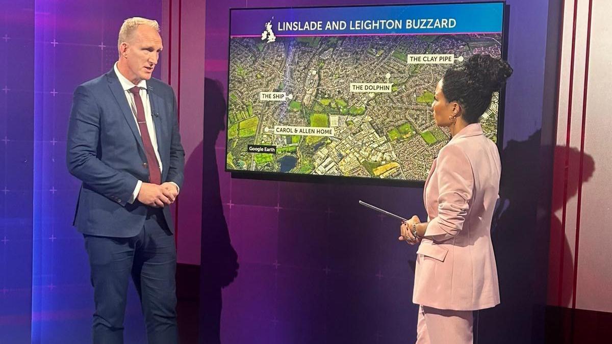 Det Insp Richard Stott is tall with grey hair and a navy suit. He is talking with Michelle Ackerley, the presenter of Crimewatch Live on the set of the show