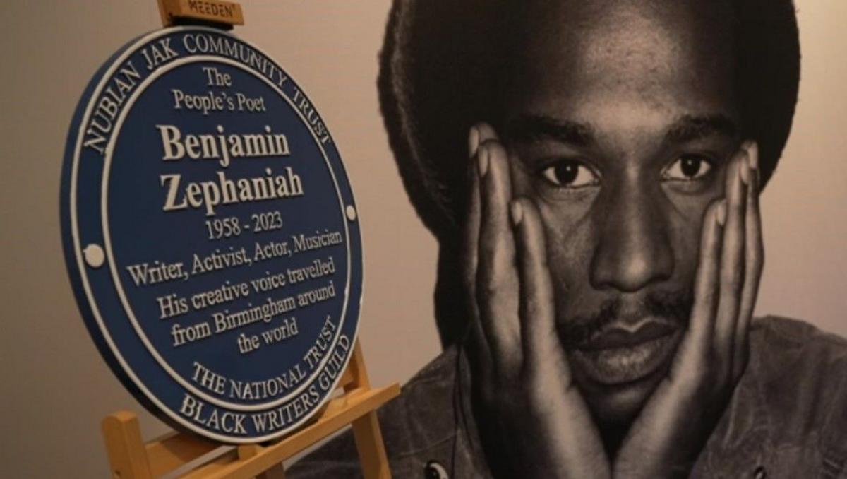 A plaque rests on a wooden frame with a black and white photo of Zephaniah as a younger man with his hands on his face.
