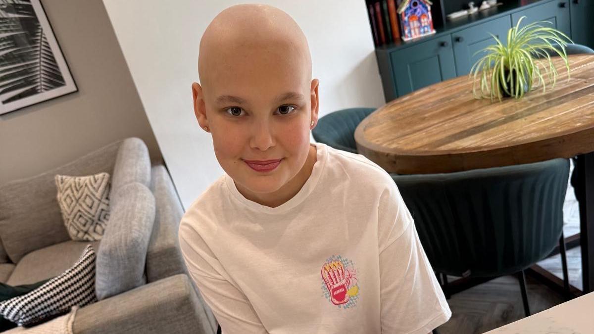 A girl who has no hair following treatment for chemotherapy, smiling at the camera