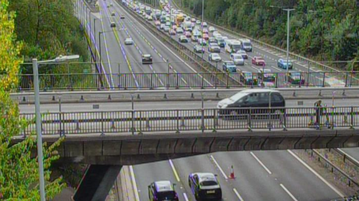 The north and southbound carriageways of the M6 motorway where the collision occurred. One side is full with traffic, the other has a few vehicles travelling on it with cones protecting some lanes.

