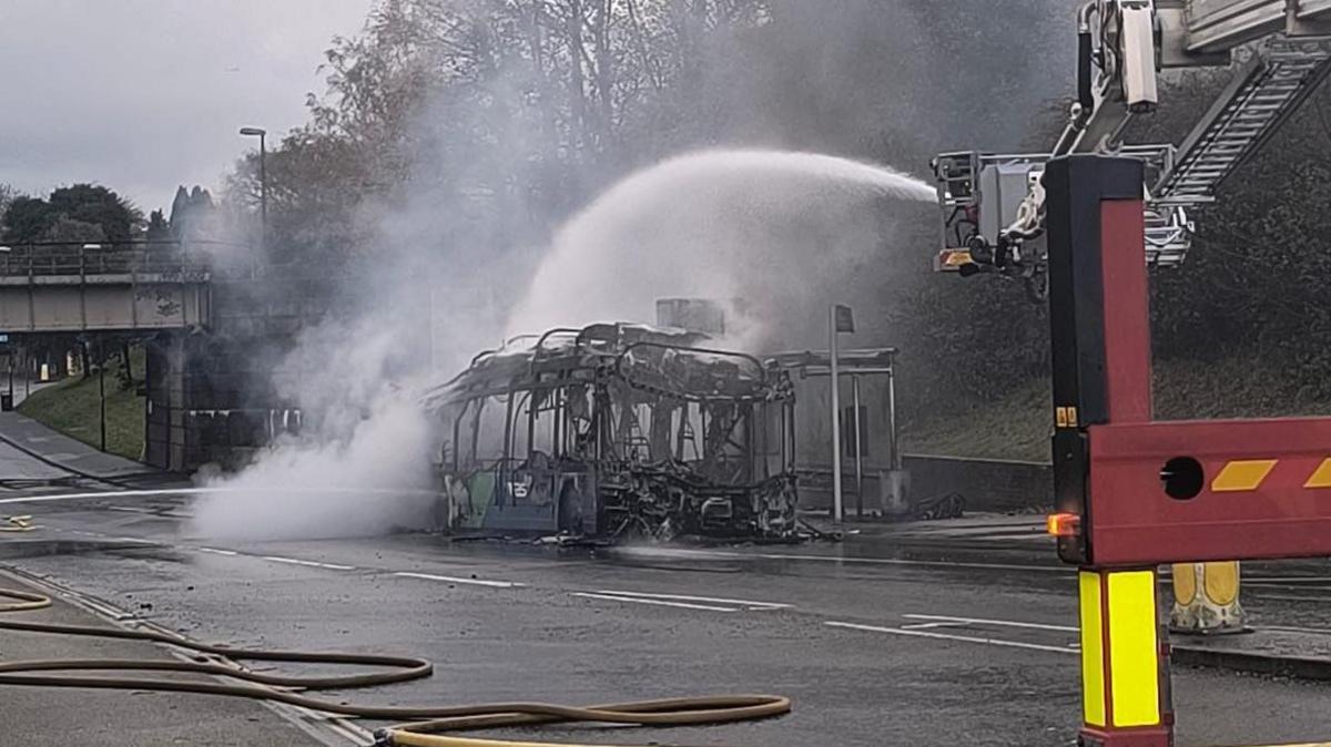 A fire tender hoses down the metal skeleton of a burnt out bus in Crawley.