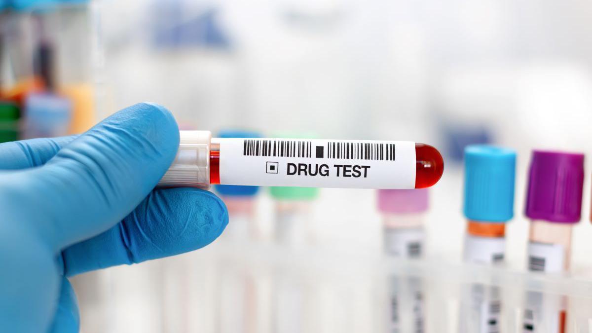 A blue glove holding a drug test sample with a red substance inside.