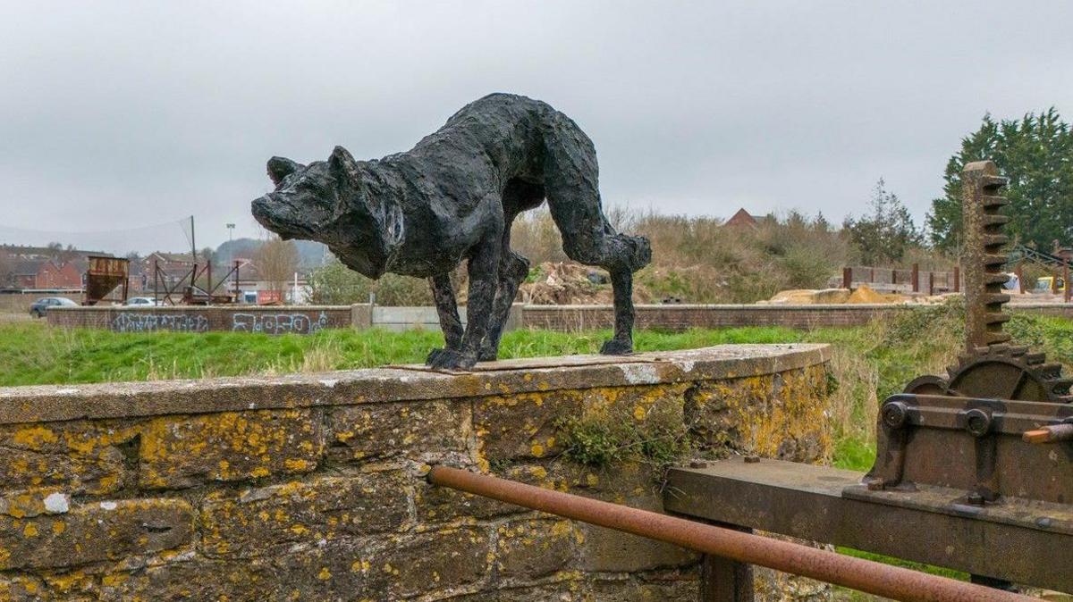 The stalking dog sculpture on top of the wall above the weir at Bridport.