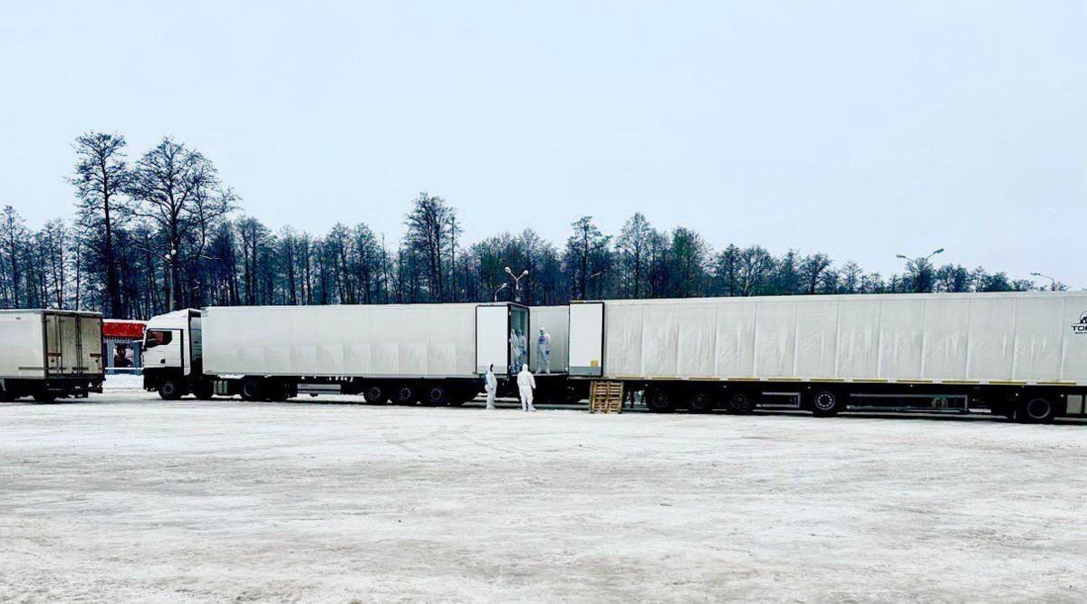 Two white trucks seen on snowy ground with individuals dressed in biohazard suits standing in the back of one