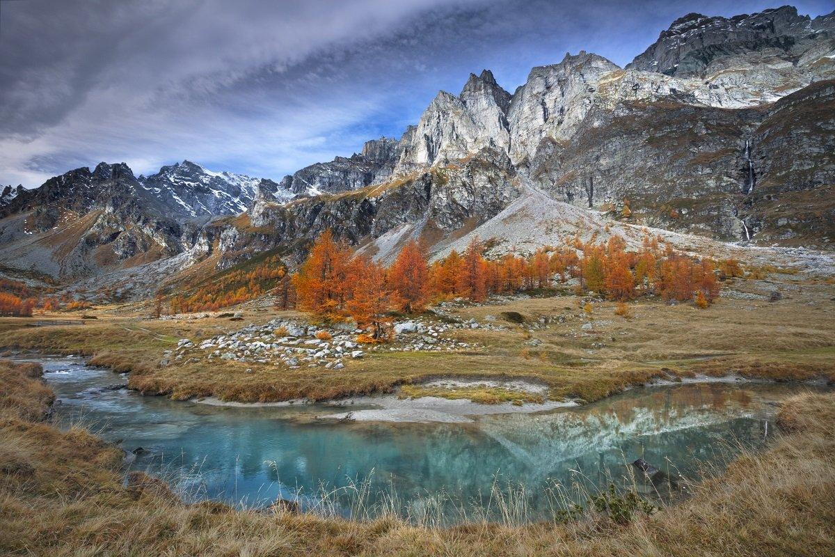 A rocky mountainous landscape with a river and orange trees