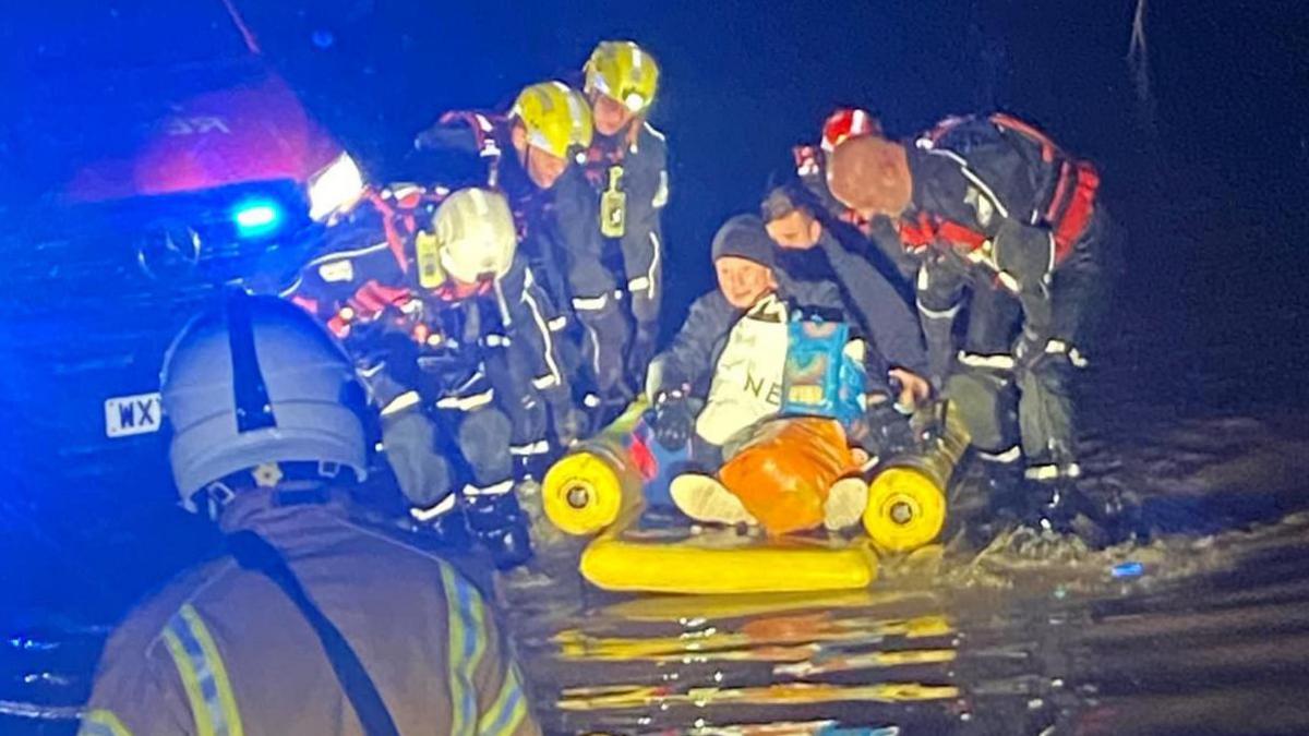 A rescue crew is helping someone onto a flotation device in flood water.