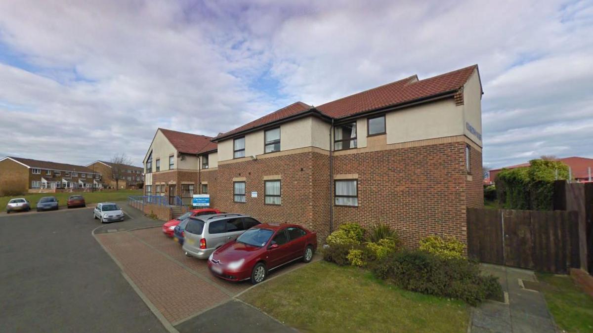 An external view of Charlton Court Care home. A number of cars are parked in its car park.