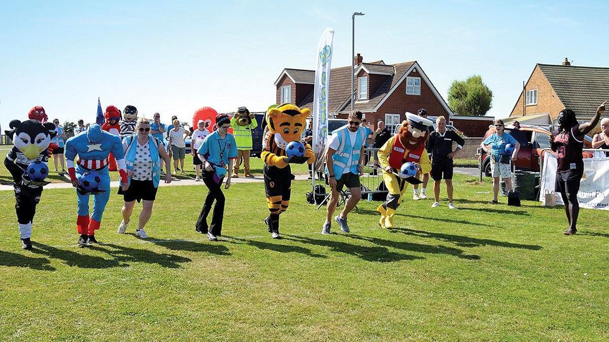 A group of people, some in fancy dress racing with footballs.