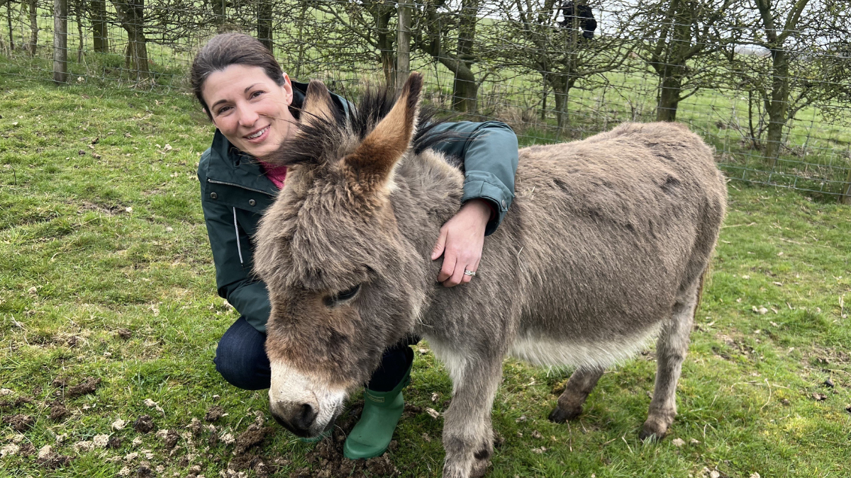 Nicola Baker crouched next to a light brown donkey