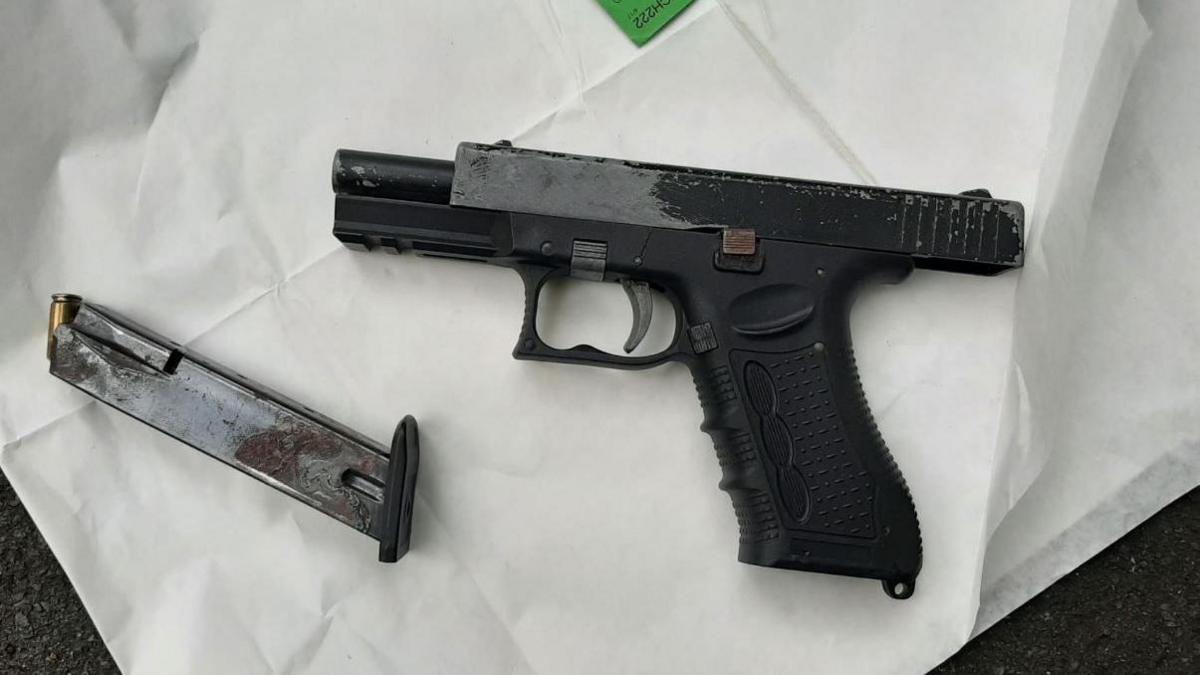 Black handgun placed on white paper- with an ammunition magazine with a bullet showing at the top on the left.
