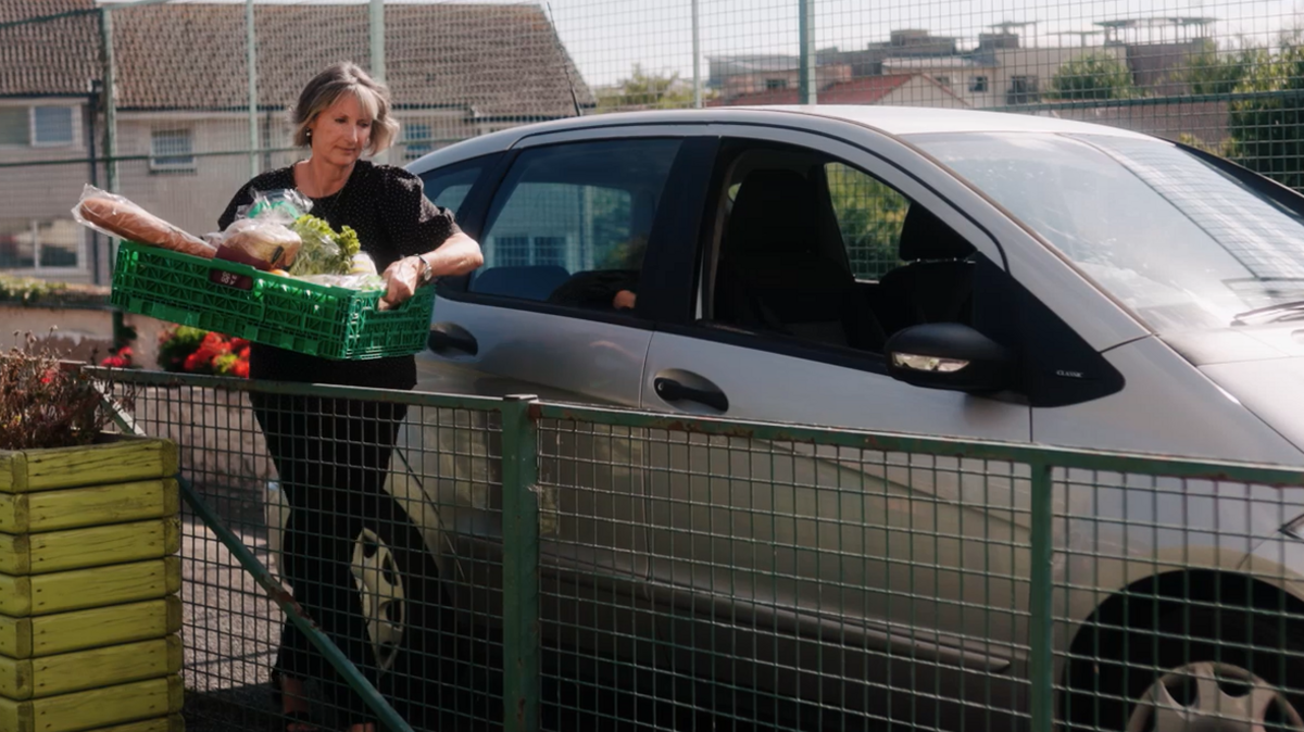 A lady carrying food shopping walking away from a car