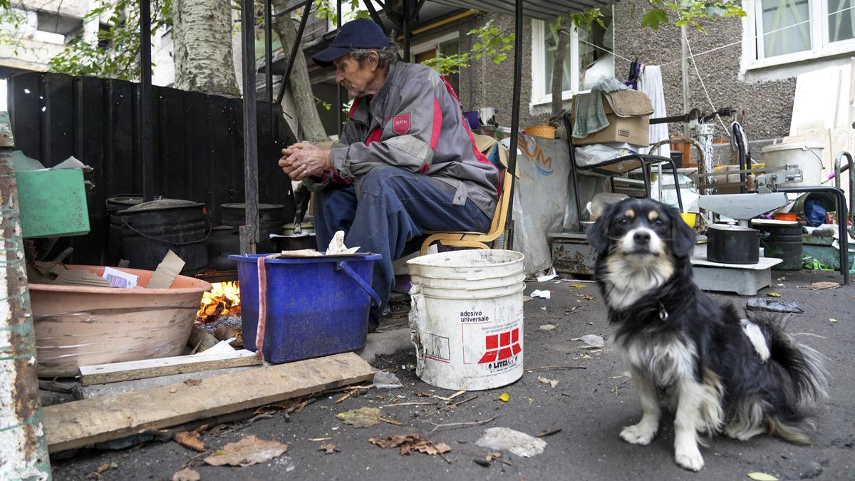 A dog sits near a man keeping warm by a fire in Mariupol - 29 September 2022