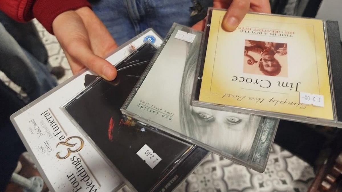 Three CDs and a DVD in the hands of a customer at a charity shop. 