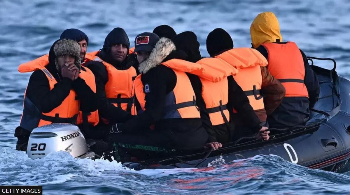 About 12 men in a small dinghy wearing life jackets