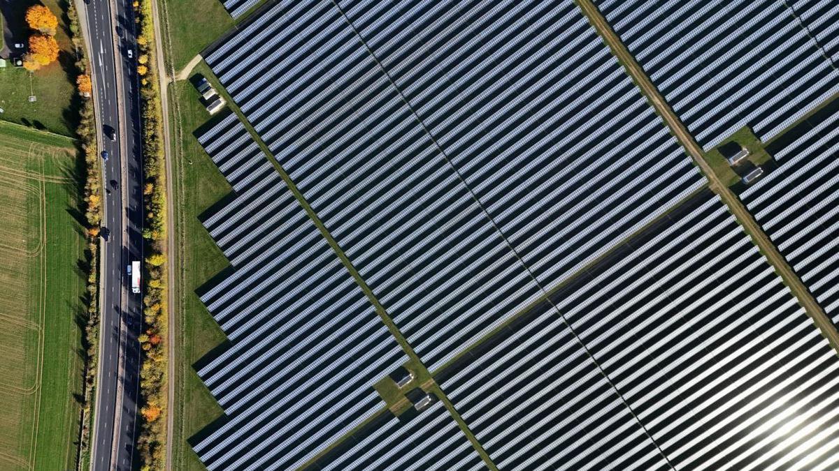 A picture made with a drone shows a large-scale solar farm with rows of panels next to a road.