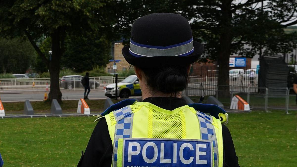 A generic police officer wearing a yellow high-vis jacket with a blue patch that reads: Police in white capital letters and a blue background.