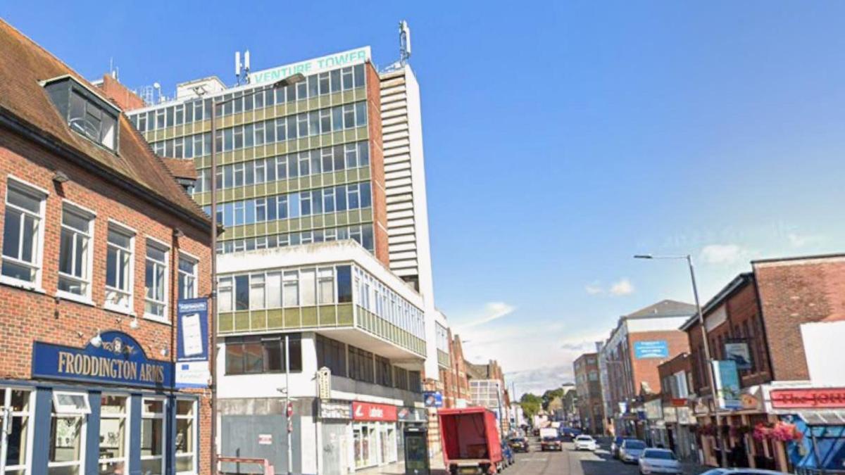 A street view image of venture tower. It looks very dated and is elevated above ground floor shops.