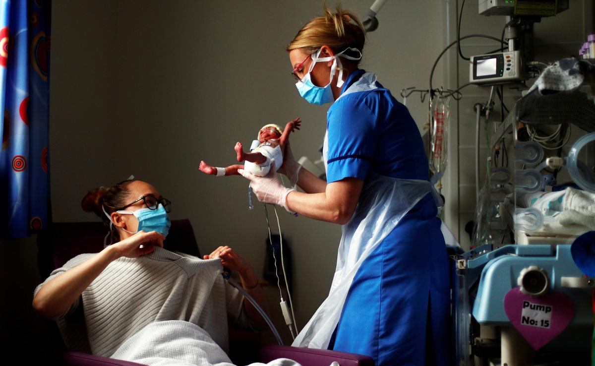 Neonatal nurse hands a premature baby to its mother in hospital