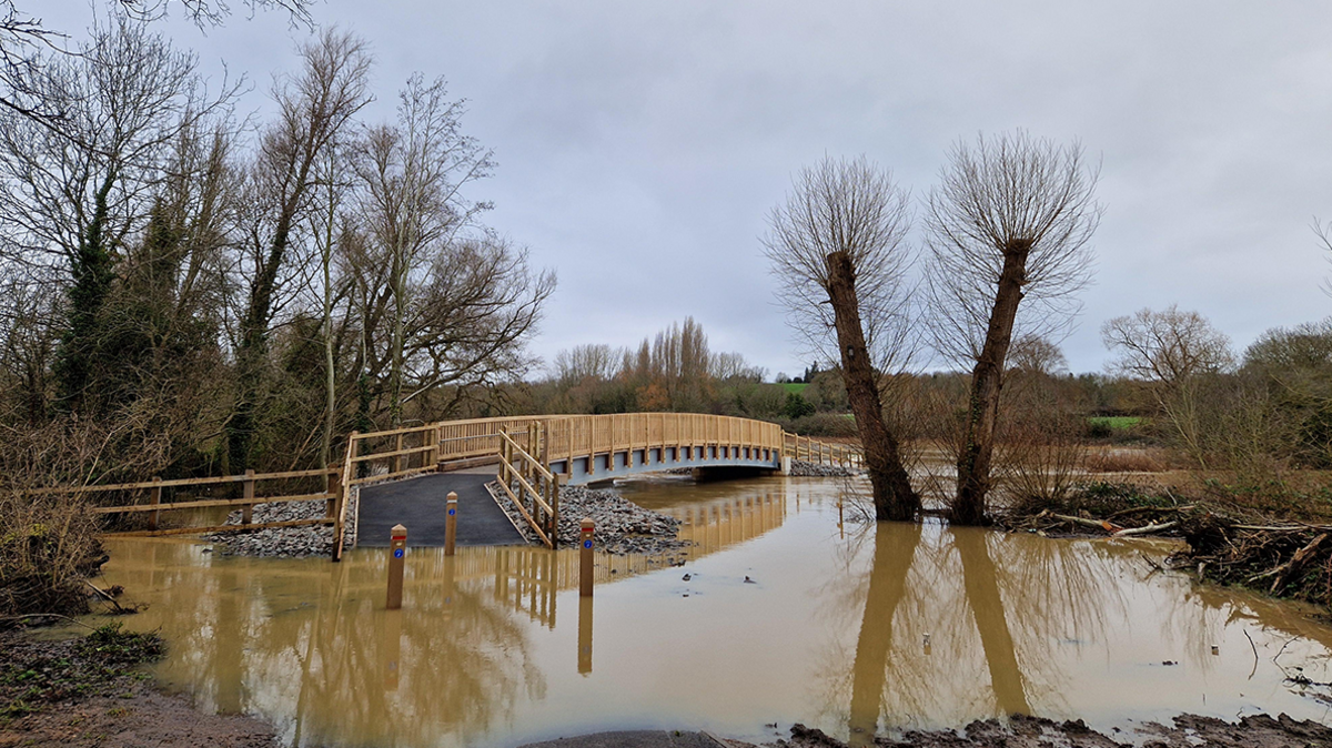 Muddy water covers the path leading to a footbridge in Leamington Spa after a waterway breaks its banks