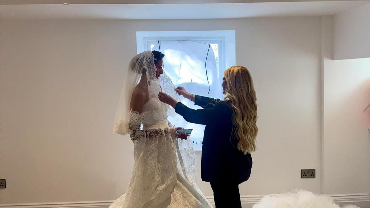 A blonde woman styling a woman in a wedding dress.