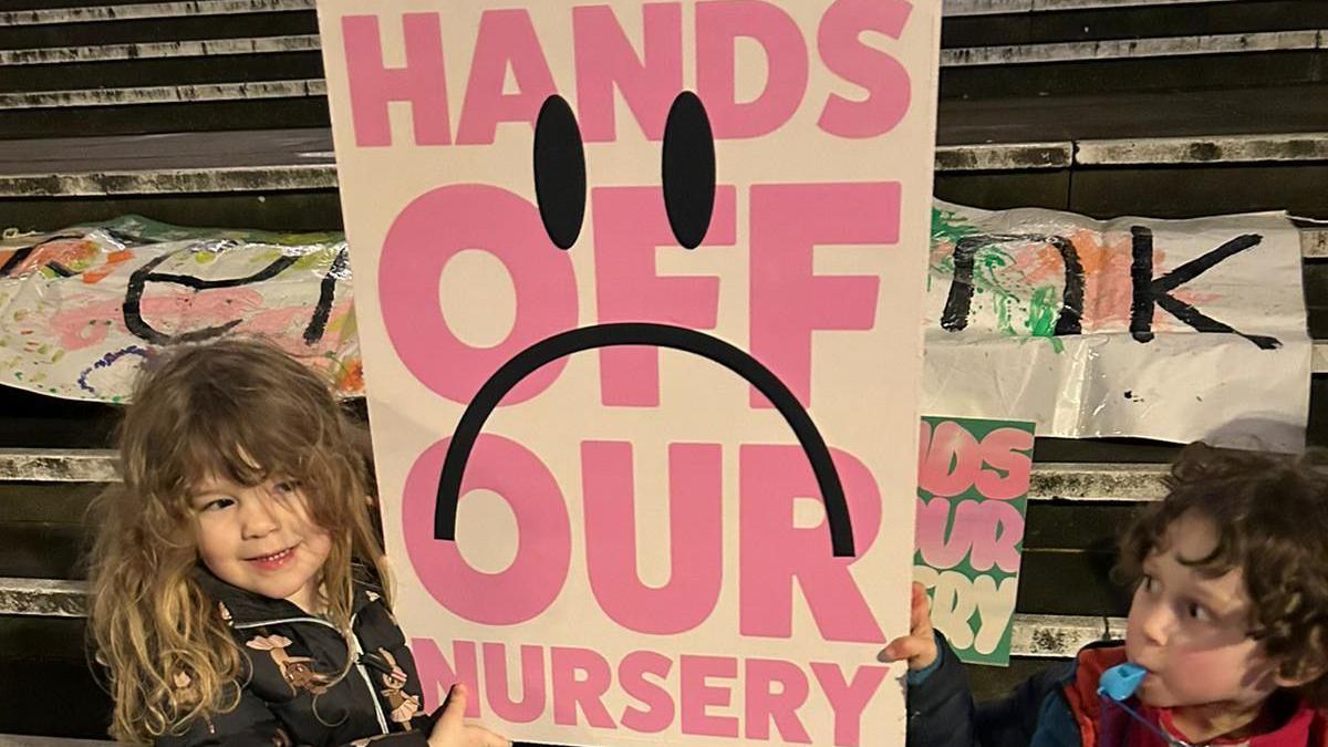 Children hold up campaign placards saying "Hands off our nursery"