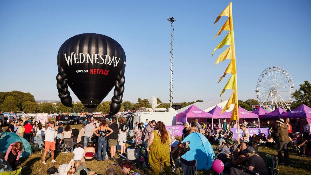 A black hot air balloon with black plaits on either side, with the words 'Wednesday, Only on Netflix' written on the front and a large crowd below.