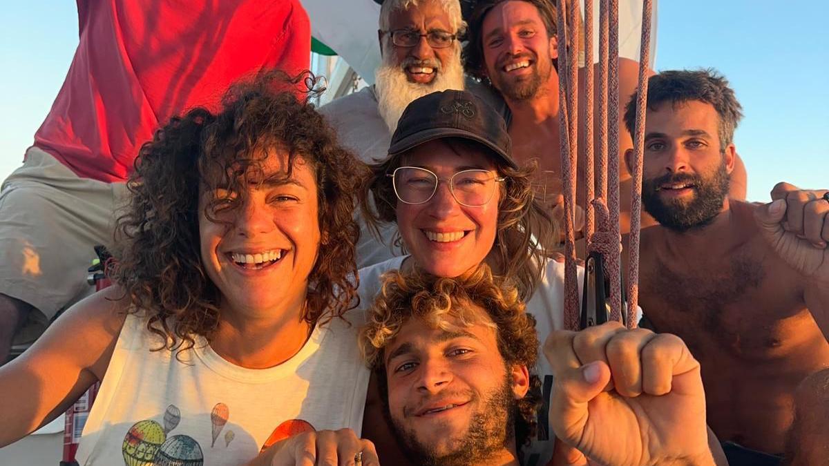 Seven people on a boat huddle together for a group photo. They are smiling in the golden glow of a sunset.