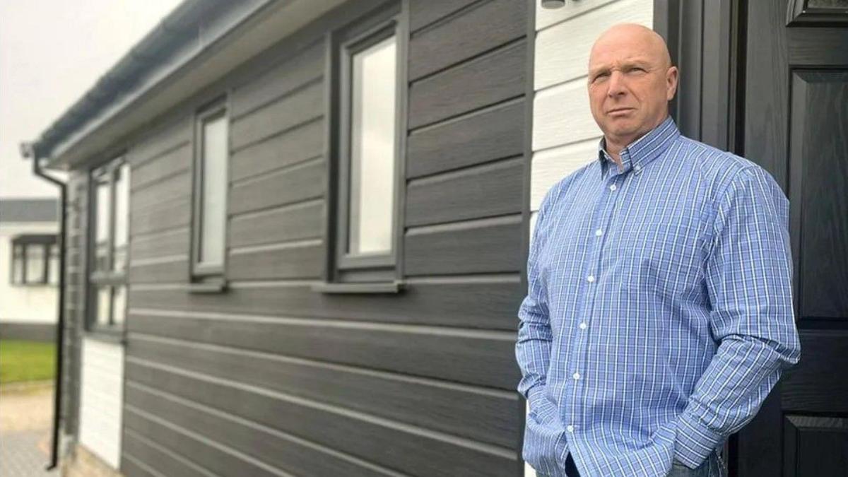 Mike Chesworth stands in front of his mobile home looking serious