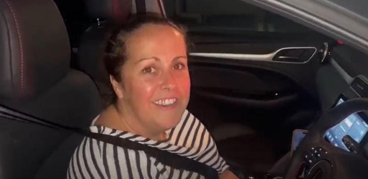 Woman wearing white and black top sitting in car.