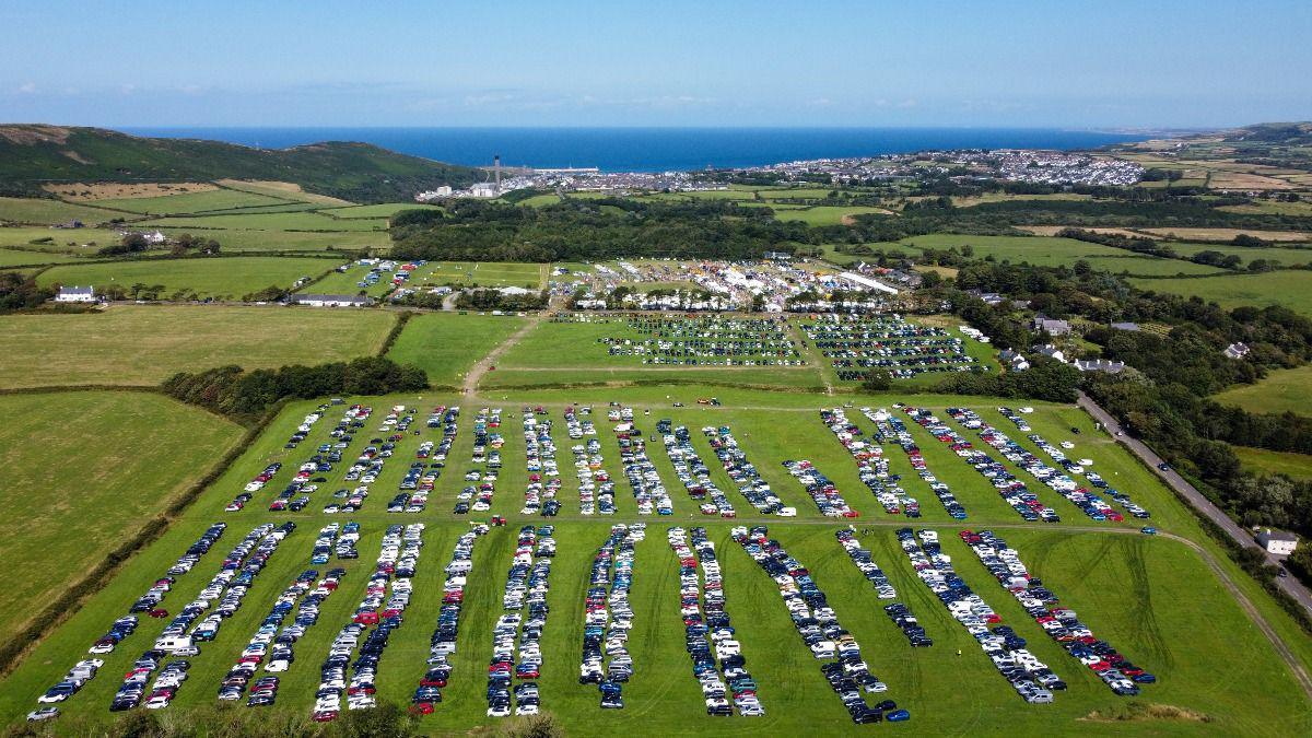 An aerial view of rows of cars parked in greens fields with the show field in the background.